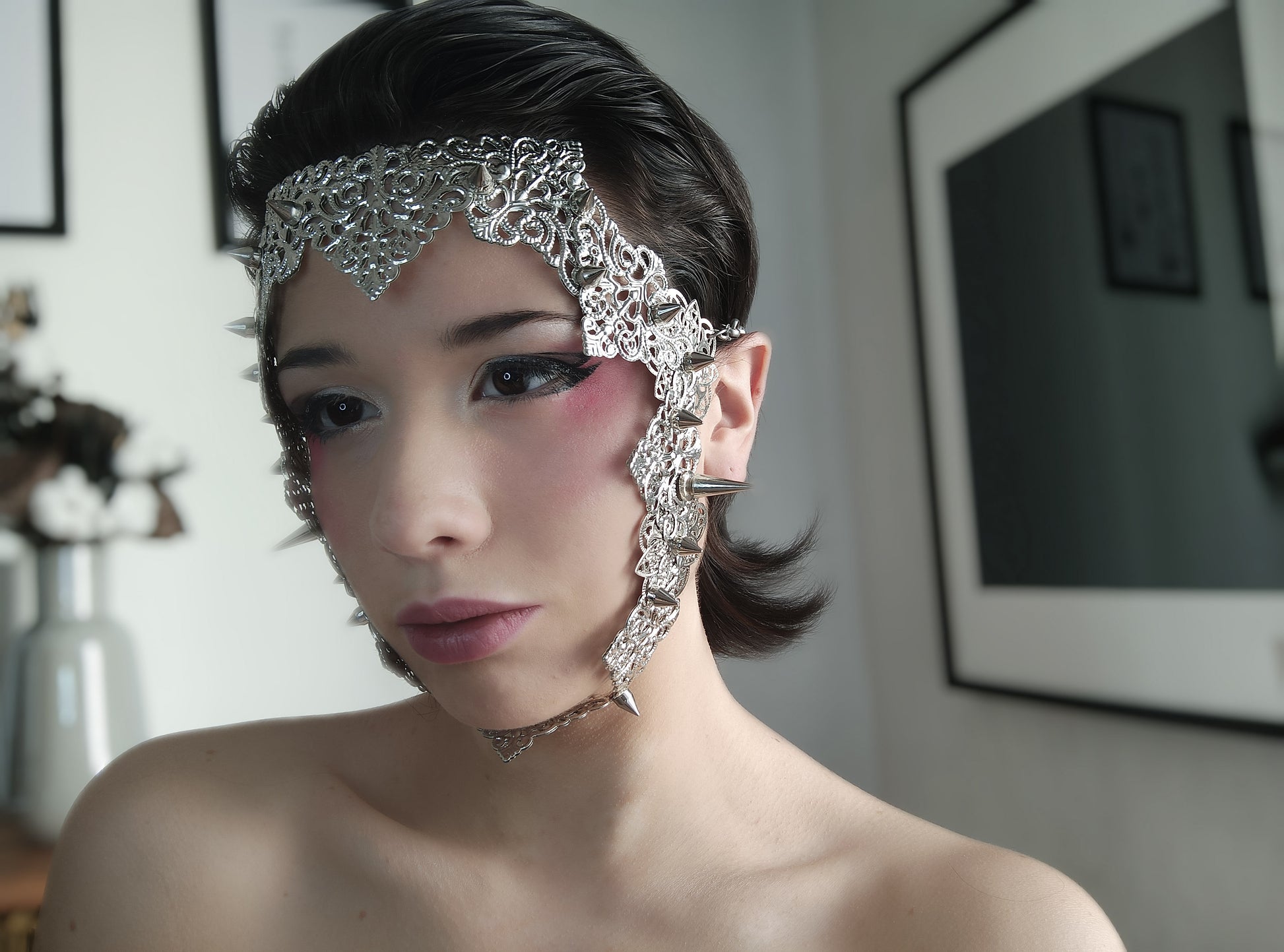 A model from Myril Jewels displays a punk filigree face frame mask embellished with studs, exuding a neo-gothic charm. This statement piece merges gothic-chic with bold punk influences, perfect for Halloween, festival wear, or adding an avant-garde edge to everyday goth style.